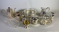 Wide view of all silver plated servingware items consisting of teapot, coffee pot, gravy boat with underplate, cream pitchers, toast rack, mustard pot, covered dish, small bowl, and collectors spoons.