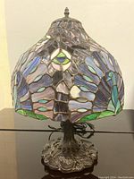 Front view of the stained glass table lamp showing colorful peacock motif with blues, greens, and purples.