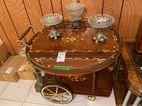 Full view of the wooden bar cart showing the brass railing, floral inlay, and wheels.