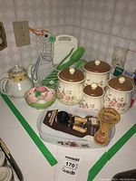Overview of ceramic canisters, green plastic utensils, pink bowl, teapot, white dish, Florida spoon rest, and packaged wooden utensils