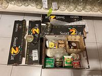 Photo showing open box with assorted canning jar lids in various packaging including Sweet 2 Eat boxes and plastic bags.