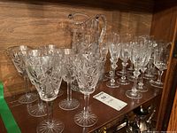 Shelved crystal wine glasses, flutes, and jug showing cut patterns and overall lot contents