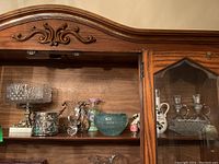 Wide shot of shelf with glass and ceramic items including compote bowl, candlestick candle holder, cruet, vase, and art bowl.