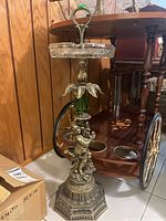 Full view of vintage glass ashtray on an ornate metal pedestal base showing figure and floral details and green glass accent.