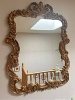 Front view of gilt composite wall mirror showing ornate rococo-style frame and rectangular beveled glass.