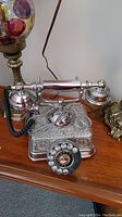 Full view of the vintage silver rotary dial telephone on a wooden surface, alongside a decorative lamp.