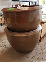 Two ceramic planters stacked, showing size and shape, the upper planter is a darker brown glaze.