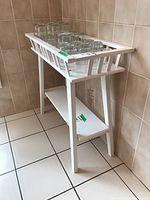 Side angle view of the white wooden shelf showing slatted sides and lower shelf, with glassware on top (not included).