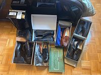 Overhead photo showing six pairs of men's leather shoes and boots of various styles, sizes, and colors, arranged in shoeboxes on the floor.