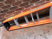 Orange step ladder laid horizontally showing front angle with black plastic foot and silver metal supports.