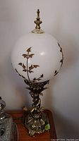 Full view of vintage metal lamp with white glass globe shade and floral metal accents, showing lamp base and finial on top