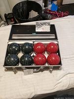 Bocce ball set with red and green balls in aluminum case on white cloth background.