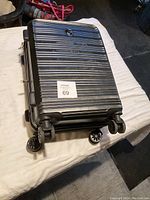 Black hard shell carry-on suitcase laying on its back, showing four spinner wheels and HEVS logo on top.