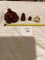 Four carved Buddha figurines arranged in a row with a measuring tape for scale and a lot number card.