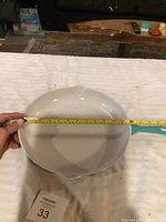 Top-down view of the cast iron pan showing the round coated cooking surface, light blue handle, and one pouring spout, with measurement tape indicating about 12 inches diameter.