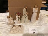 Five Willow Tree collectible figurines displayed upright on a surface in front of a box. Includes multiple mother and child themed figures and one wall plaque. Neutral colored resin figures with smooth, hand-carved style.