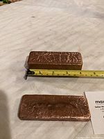 Two solid copper bricks on white cloth background with measuring tape showing length about 5 inches.