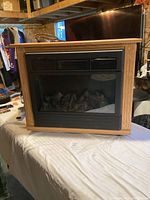 Electric fireplace insert within wooden mantel on table, showing full front view with realistic log bed behind glass.