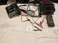 Photo showing the full lot of electronic items including two battery chargers, a handheld work light, a multimeter, and connecting cables with clamps