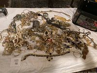 Wide shot of assorted tangled jewelry on a white cloth, includes gold and silver chains, earrings, and bracelets