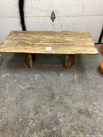 Front view of a rustic live edge wooden coffee table showing the wood grain and three legs on a concrete floor.