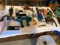 Overview of all tools laid out on a white cloth surface including drills, nail guns, electric drills, and measuring tools.