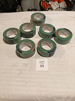 Seven rolls of green RONA painter's tape arranged on white table.