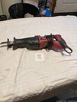 Full view of Skil Model 9216 reciprocating saw laid flat on surface showing red and black housing, cord wrapped around body, blade attached at front.