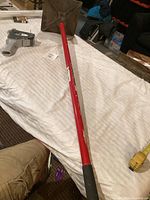 Full view of ground tamper showing red handle and square metal tamper base on a white cloth surface.