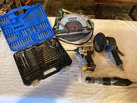 Wide shot of the lot showing Ryobi circular saw, DeWalt cordless drill, drill bit sets in blue and black cases, and several air pneumatic tools.