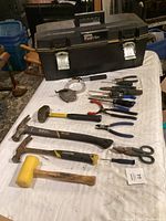 Complete layout of tools and toolbox on white cloth, showing toolbox, hammers, pliers, scissors, and screwdrivers.