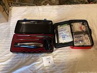Overview photo showing the black carrying case with the electric turkey carver and its accessories on the left side, and the open black zippered first aid kit case on the right side with various medical supplies visible.