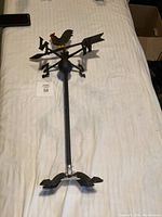Top view of the assembled cast iron weather vane with rooster, arrow, and directional letters on a white surface.