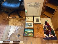 Full overview of all lot items on floor including scroll map, framed prints, carved wooden map, tapestry