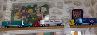 Five collectible model trucks displayed on a high shelf against a Campbell's Soup wallpaper background, showing colorful branded trailers and cabs.