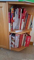 Image showing two shelves in a wooden cabinet holding approximately 17 Campbell's Soup cookbooks and collectibles books, arranged upright.