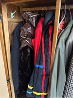 Photo of assorted coats and jackets hanging in a wood wardrobe, showing brown leather-like coat, a red and black striped wool coat, and green jacket.