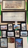 Wide view of 11 framed art prints arranged on a wall. Includes detailed landscapes, cityscapes, architectural prints, and a historic map. Frames mostly black/dark wood, varying sizes up to 12x24 inches.