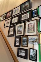 Photo capturing sixteen framed signed prints arranged on a wall, showing variety of styles and frames.