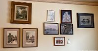 Wide view of nine framed art pieces hung on a wall showing various landscapes, cityscapes, and nature scenes.