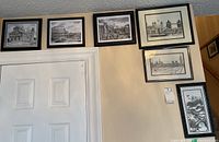 Six framed black and white architectural prints arranged on a wall above a door, depicting various iconic buildings and scenes in monochrome style.