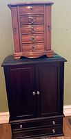 Two jewelry boxes stacked, larger black floor standing box below smaller brown wood tabletop box