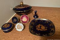 Limoges porcelain dish set with oval lidded dish, small plates, and small pitcher all decorated with gold gilded patterns on blue, pink, and white backgrounds.
