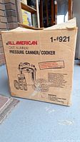Original cardboard box labeled “All American Cast Aluminum Pressure Canner/Cooker 1-#921”