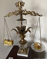 Full view of the brass and crystal balance scale with two glass hanging pans, showing scale details and size comparison with hand.