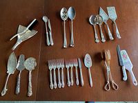 Overhead view of an assortment of silver plated serving utensils and flatware laid out on wooden surface.