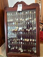 Full view of the wooden display case containing multiple rows of souvenir spoons.