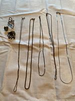 Six sterling silver necklaces and three rings laid out on white cloth surface.