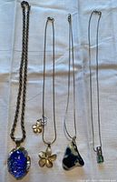 Four sterling silver necklaces laid out flat on white fabric background, showing varied pendants including glass and stone with floral charms.