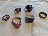 Six sterling silver rings laid out on a white fabric surface, showing different stones, shapes, and designs.